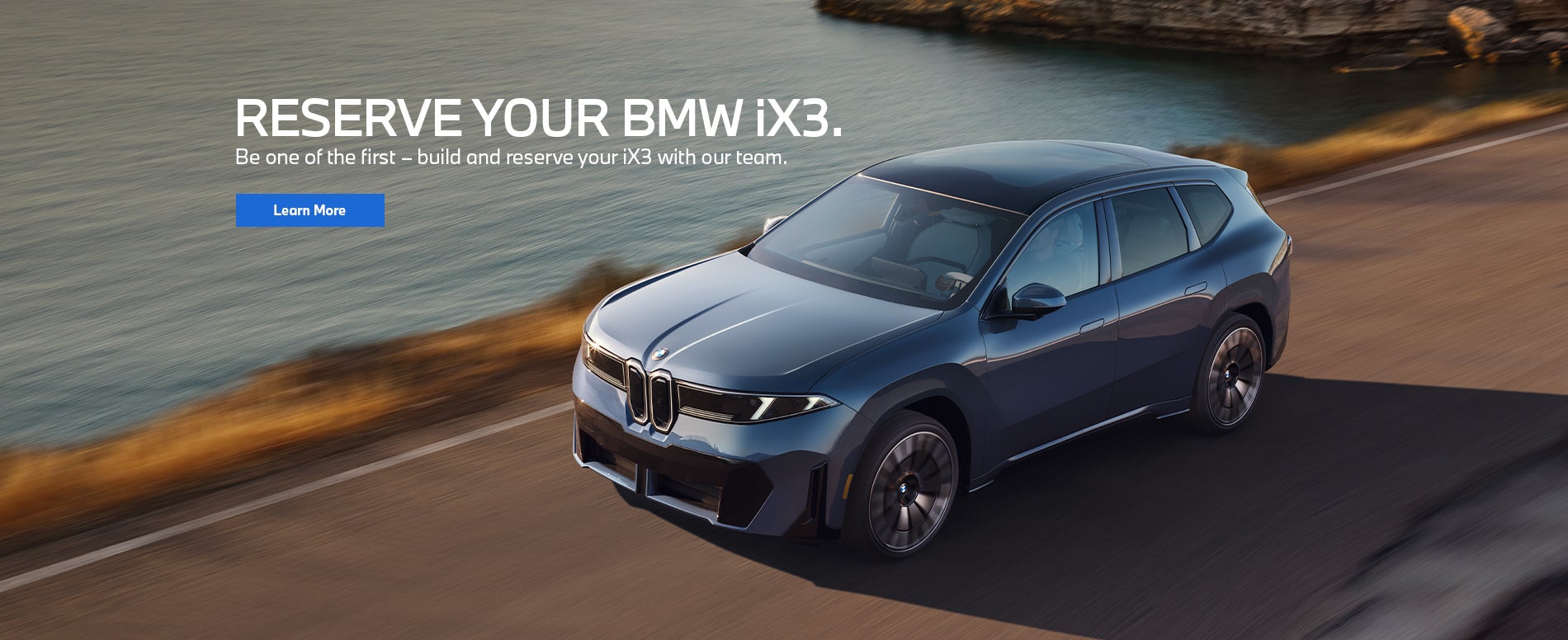 BMW iX3 vehicle driving on a road near mountains and water.